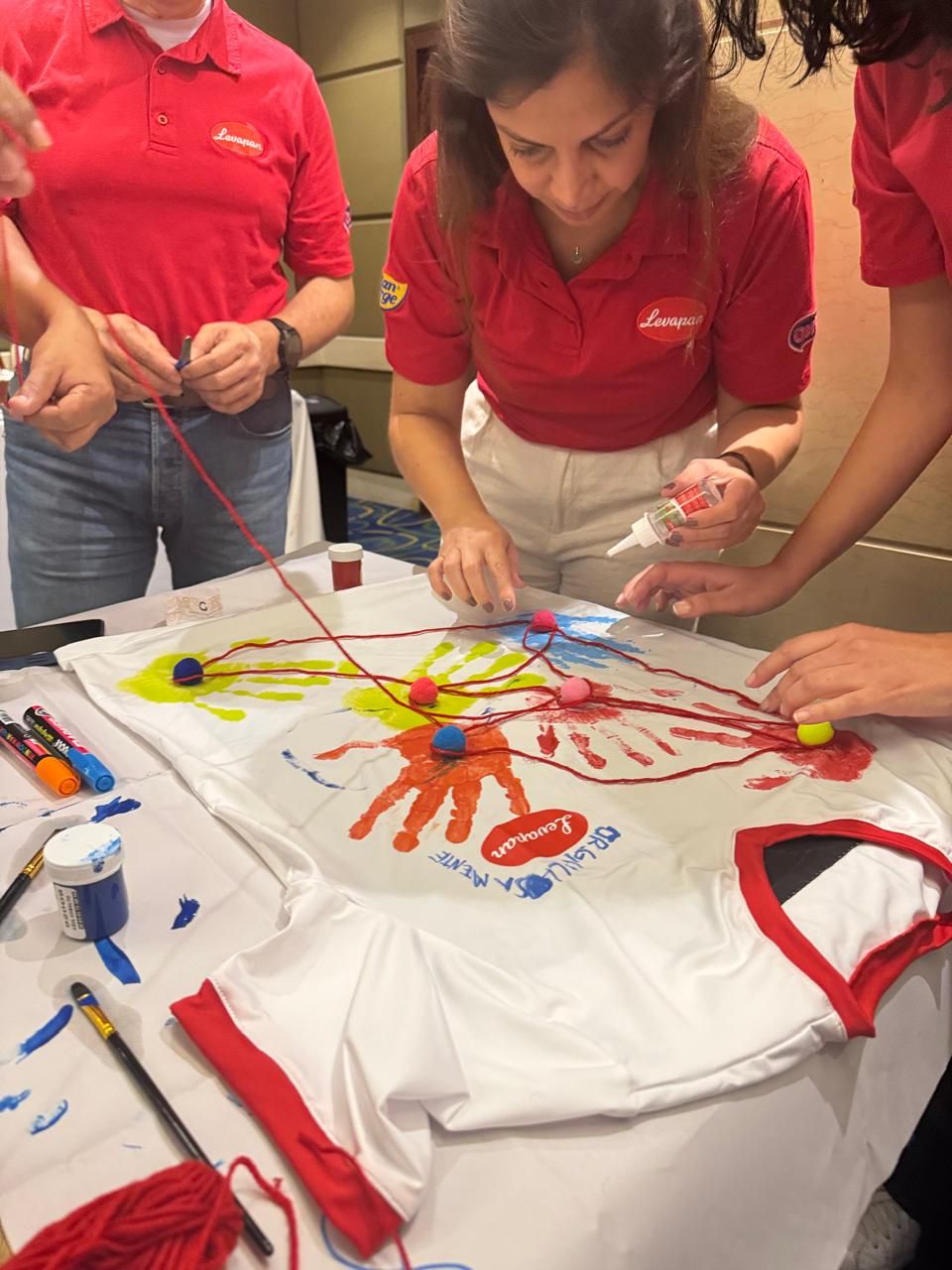 Participantes conectando con lana las huellas de sus manos pintadas sobre una camiseta
